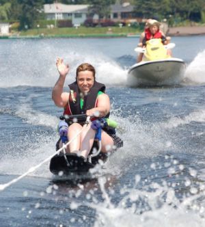 Sit-skier waves to the camera while the chase boat, with jumper, is ready to assist the skier. 